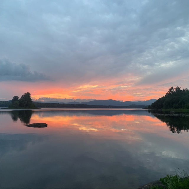 Pink and blue sky as the sun sets behind the mountains, both are reflected in smooth, still water.